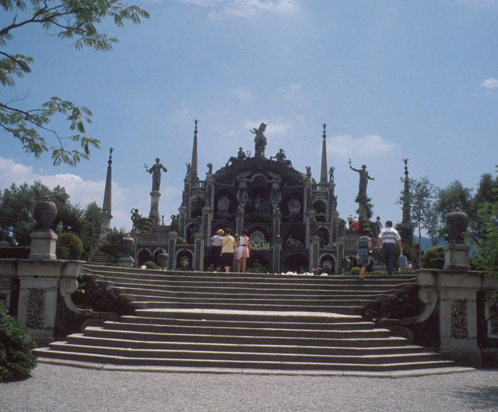 An ornate structure with columns, statues, and spires stands at the top of wide stone steps. Figures climb the steps and stand in front of the structure.