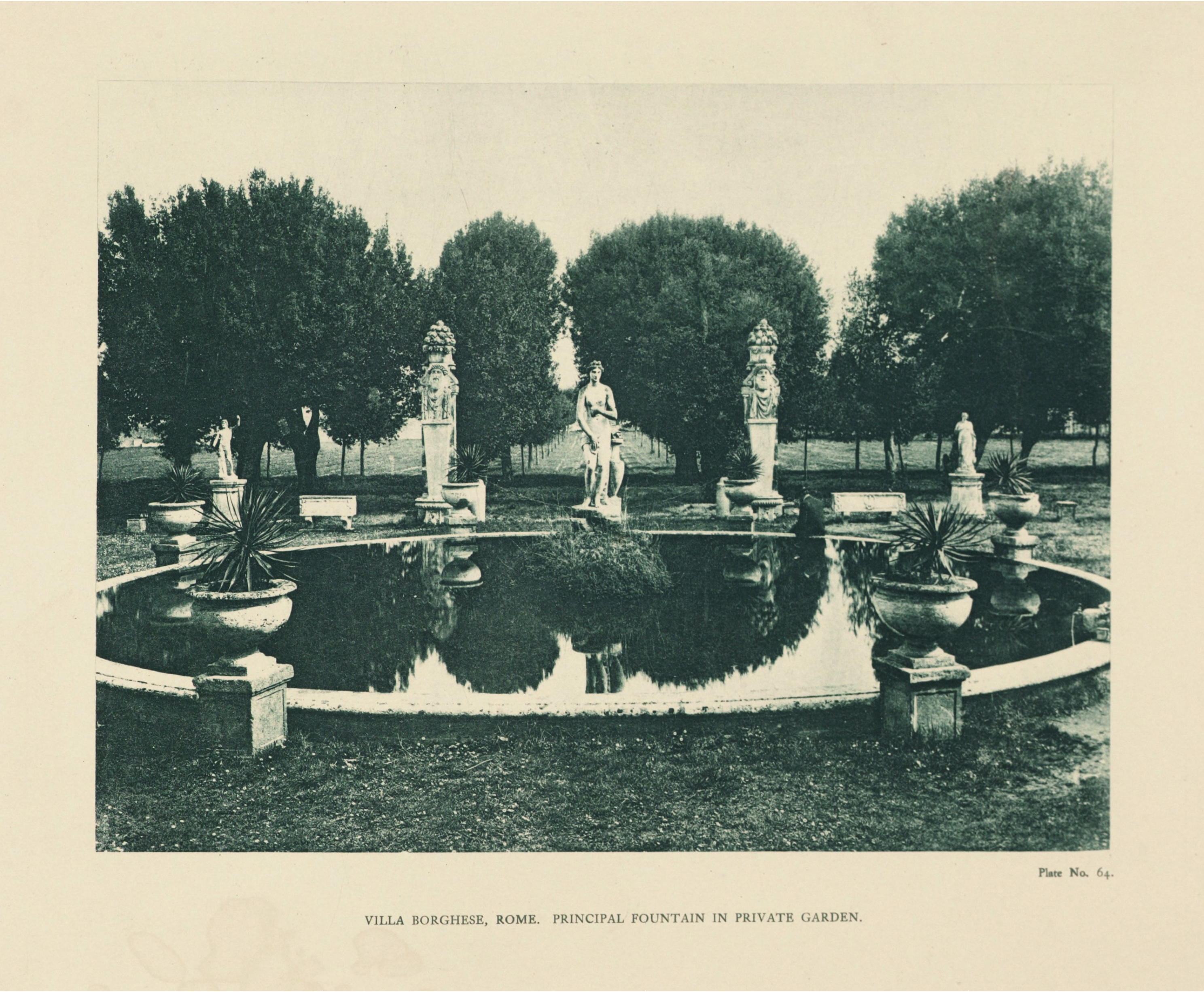 A circular fountain with a central classical female statue is surrounded by four statues and plants in a landscaped garden, with an allée of trees in the background.