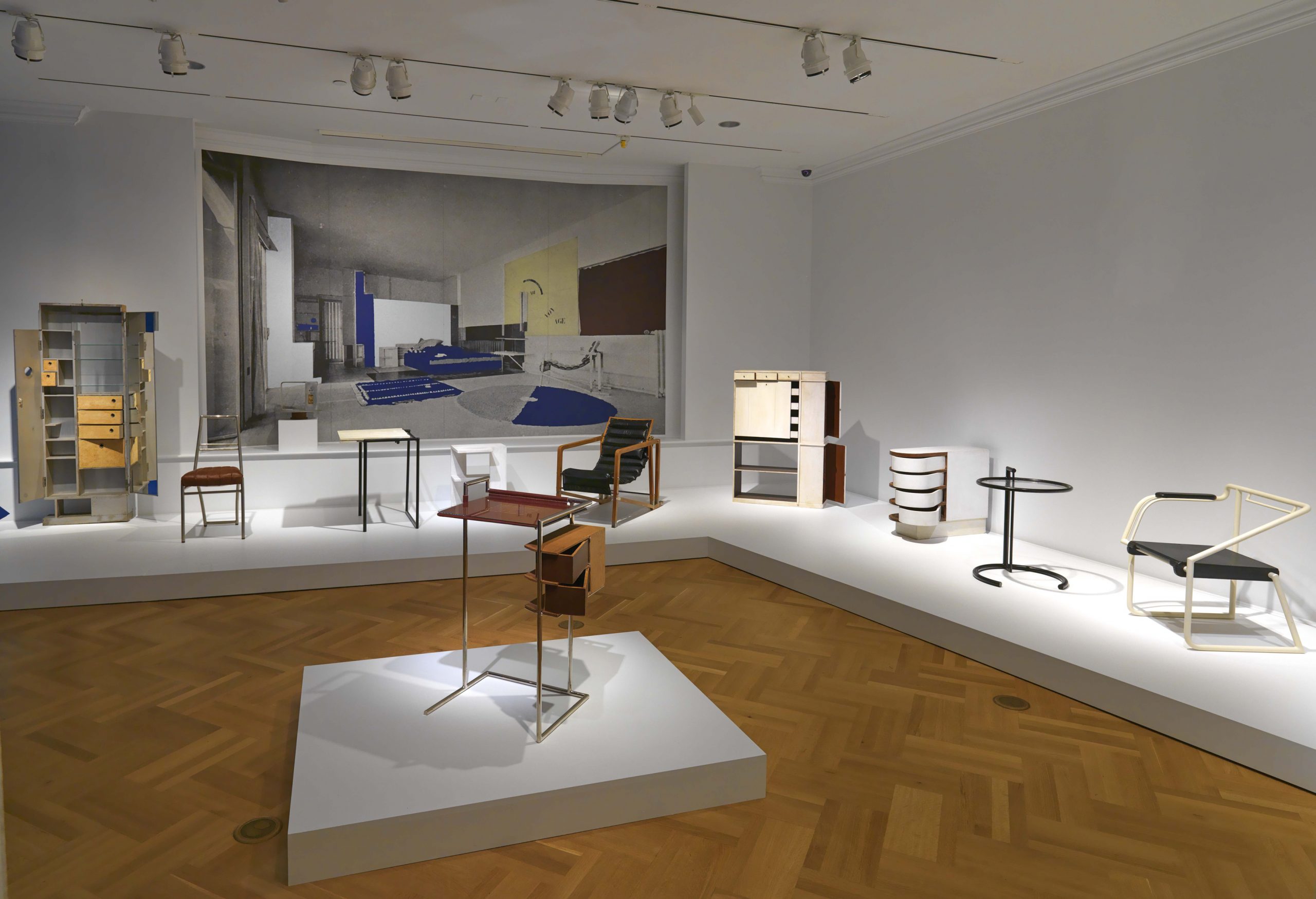 Exhibition image of table on central pedestal and multiple pieces of furniture on platforms.