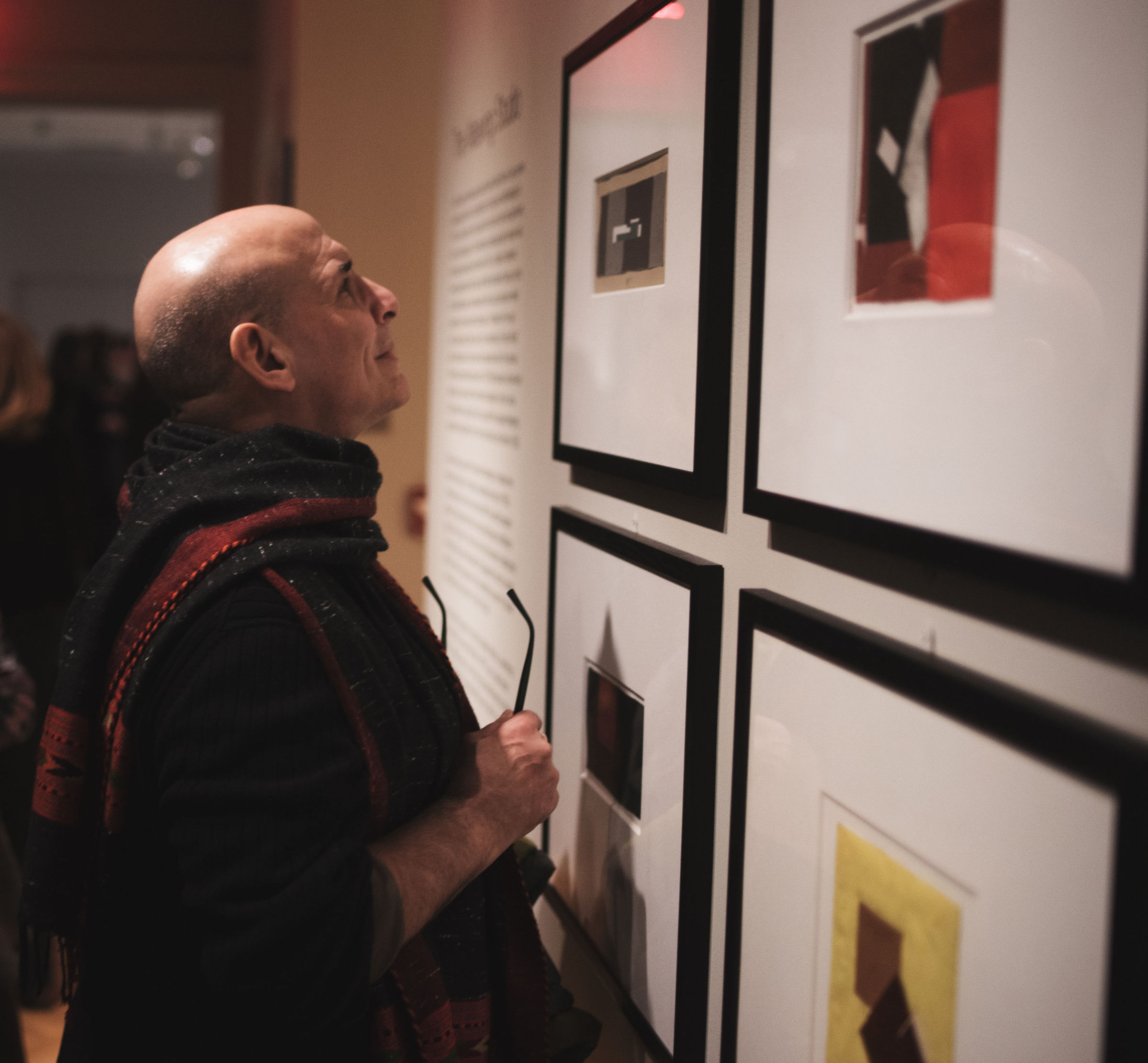 Photograph of a man examining framed works at the opening of the Eileen Gray exhibition.