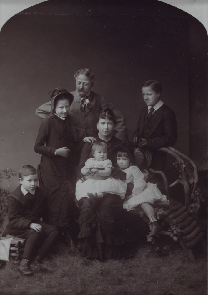 Portrait of a family with the mother seated in the center surrounded by five children and the father standing in the back.
