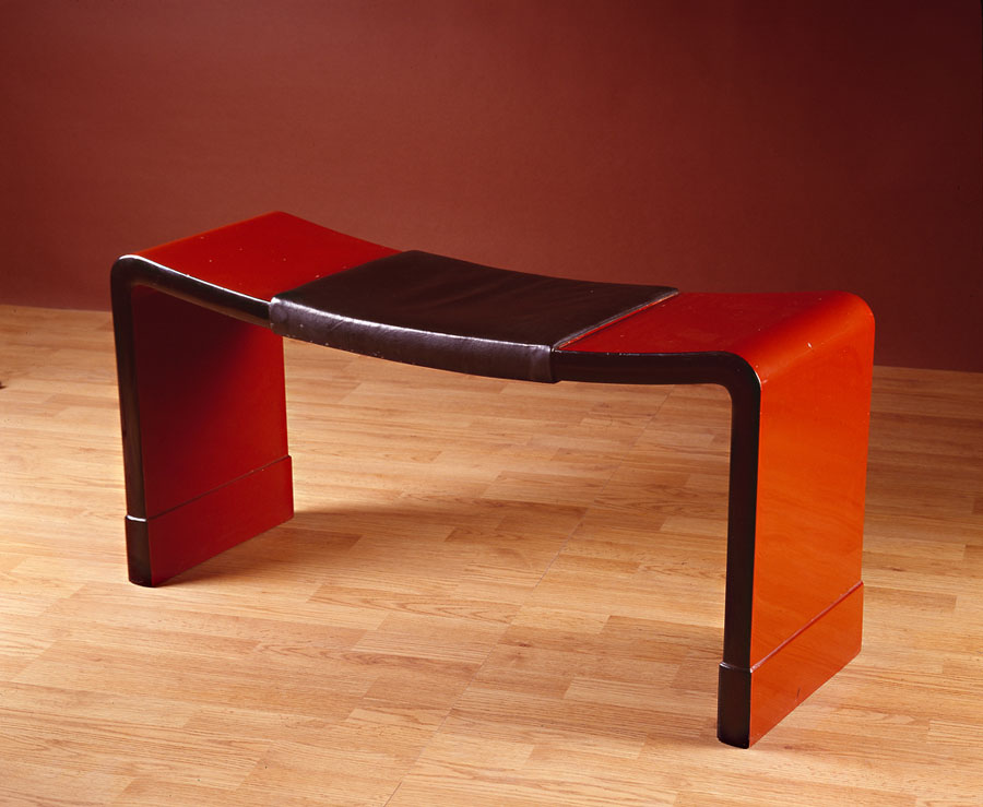 Installation image of a red lacquered banquette with a leather pad.