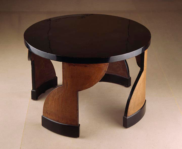 Photograph of a rounded black lacquer pedestal table with four wooden hourglass-shaped supports.