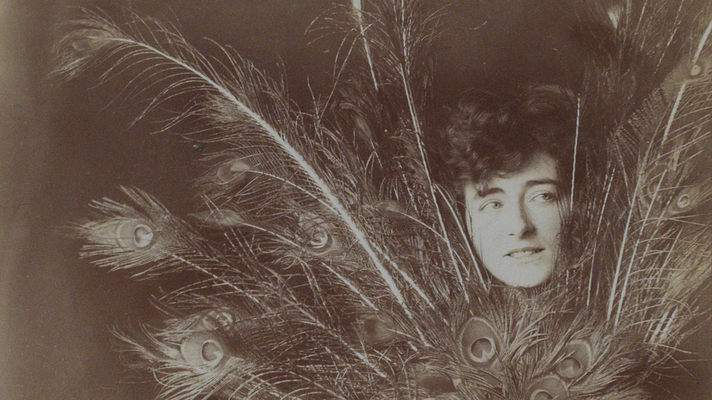Sepia-toned portrait of Gray's face emerging from behind a bundle of peacock feathers.