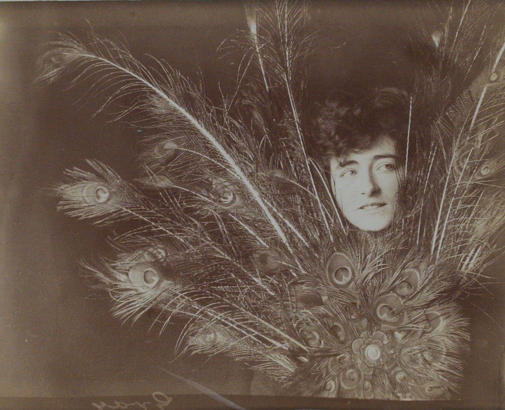 Photograph of a woman's face peeking through a large bouquet of peacock feathers.