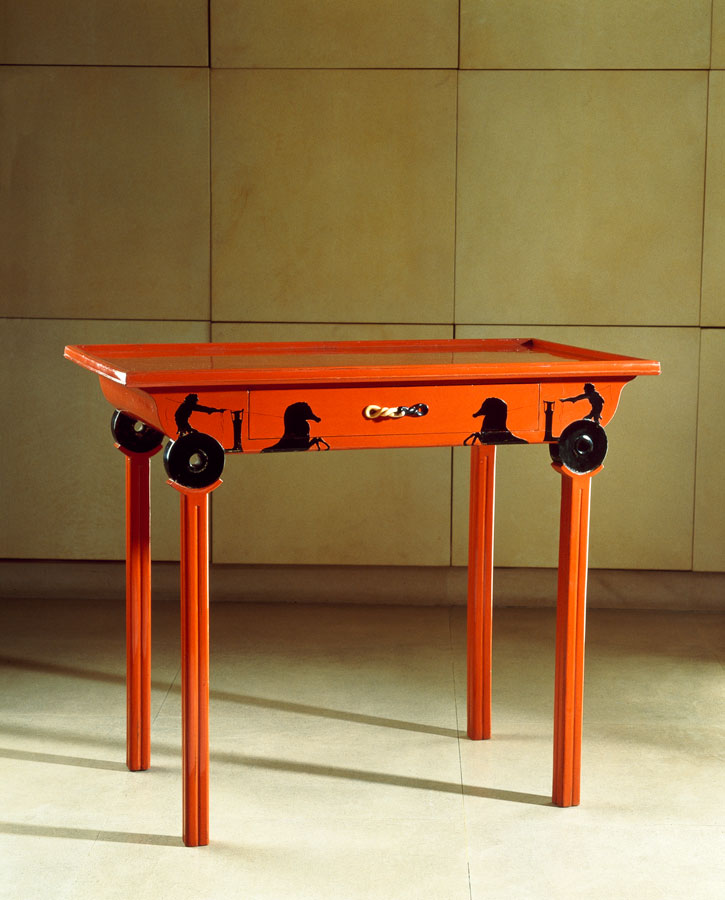 Photograph of a small red lacquered table with silhouetted men driving chariots in black decorating the top of each leg.