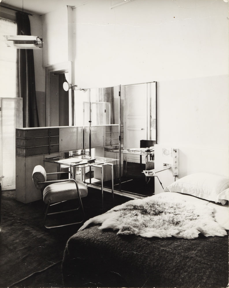 Interior view of a bedroom with a large-mirrored vanity and bed with a fur throw.