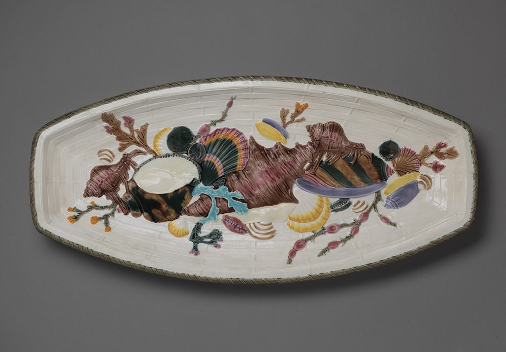 Oblong majolica dish with white woven motif ground and coral and shells of various colors.