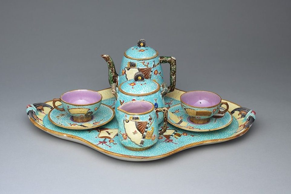 Majolica "Fan" tête-à-tête tea set with turquoise ground, brown and yellow details, and and pink interiors. Includes tea pot, sugar jar, cream jug, two teacups and saucers on large quatrefoil tray