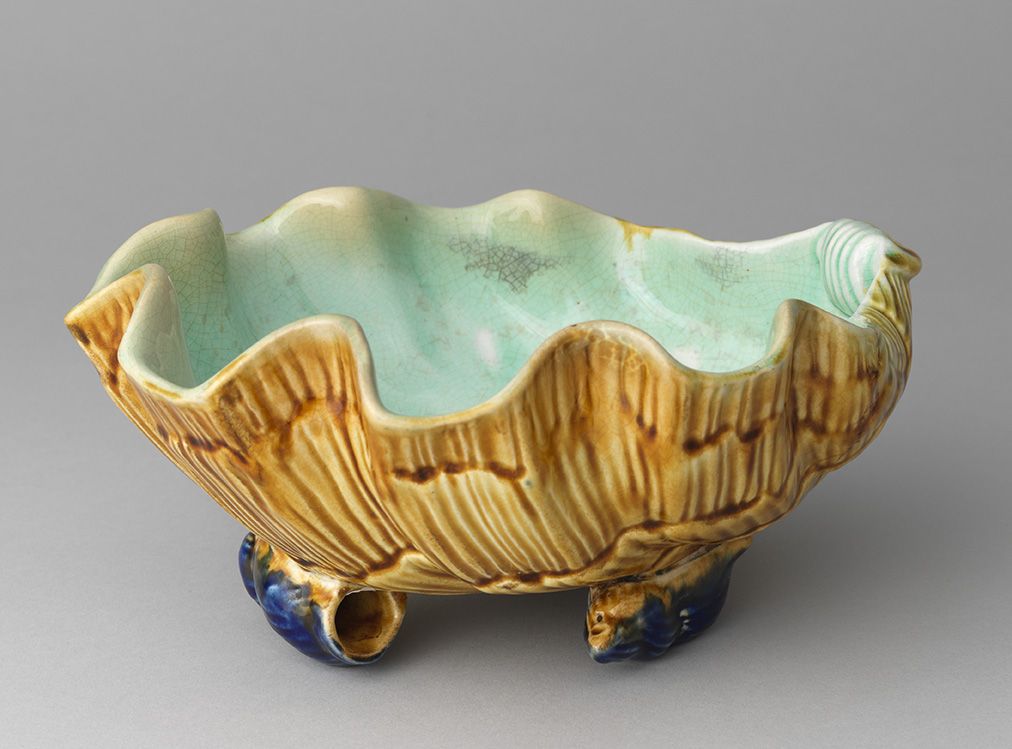 Majolica shell-shaped salad bowl on two fish-shaped feet, brown exterior with turquoise interior.
