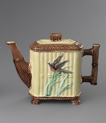 Square majolica jug with bamboo motif on lid, handle, spout, and feet. Yellow reed texture ground with scene of black and red bird and green leaves.