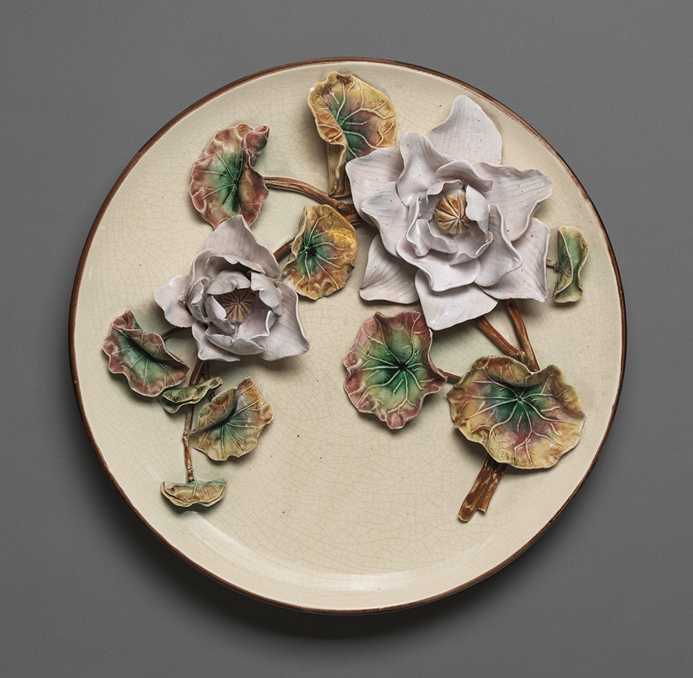 Cream ground majolica plaque with two molded lavender flowers and molded brown steam with green and brown leaves.