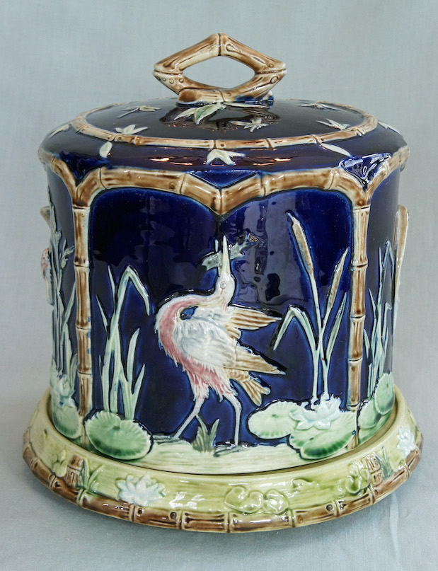 Majolica stilton cheese stand and lid. Dark blue ground, bamboo motif. Scene of stork or crane with fish in its mouth, green cattails and lily pads.