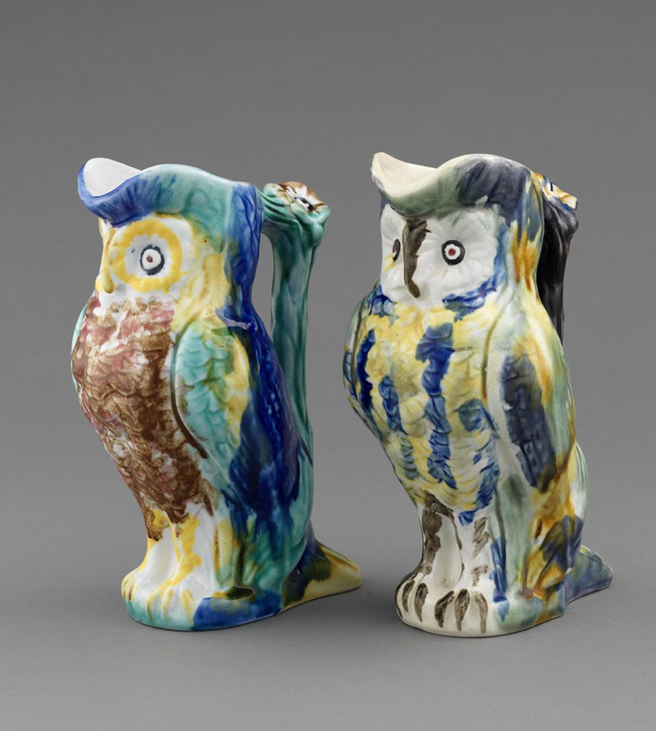 Two majolica owl jugs with branch handles, color palette of various spots of blue, yellow, green, and brown.