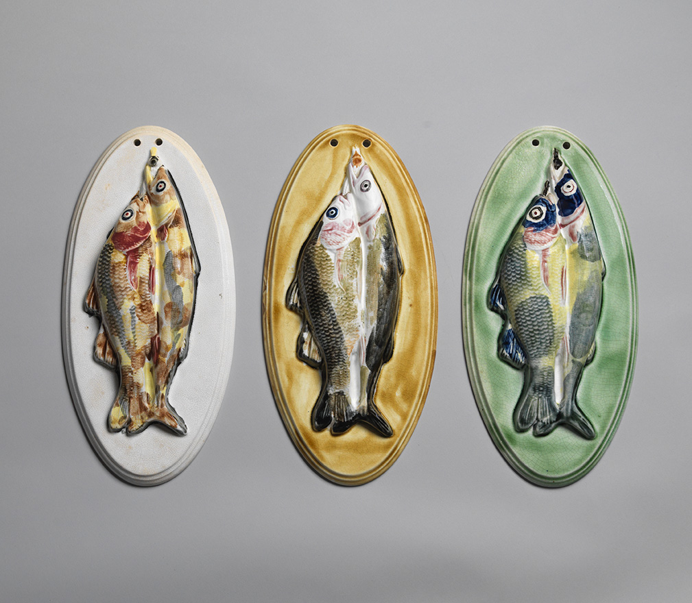 Three oval majolica plaques with two molded fish on wach plaque. Various colors, left plaeuq has white ground, middle plaque has yellow ground, right plaque has green ground.