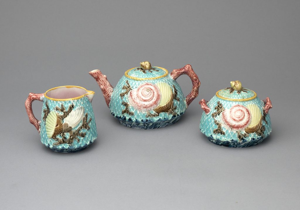 Majolica teapot, creamer, and sugar bowl in blue with a netted pattern and decorated with shells and coral. Red coral handles and teapot spout.