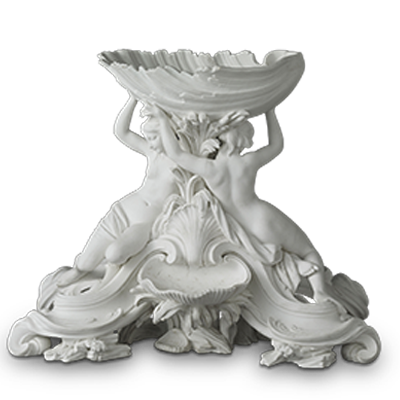 An ornate white ceramic sculpture featuring a large shell-shaped bowl supported by two sculpted female figures. The figures are depicted in classical style, with detailed, flowing drapery and intricate decorative elements at the base.