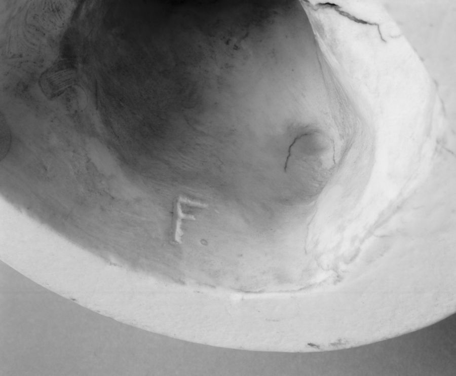 Black and white close-up photo of the inner part of a curved, rough-textured structure. The letter "F" is carved into the surface. The structure has an organic, uneven appearance and there is a visible crack near the top edge.