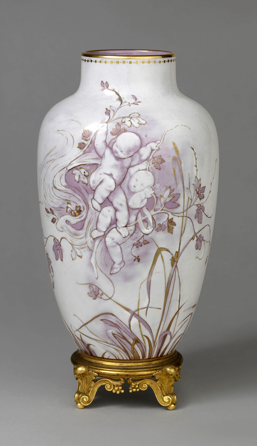 A tall, decorative porcelain vase adorned with a floral pattern featuring purple and gold hues. The vase sits on an ornate gold-colored stand with intricate designs. The background is a plain gray.