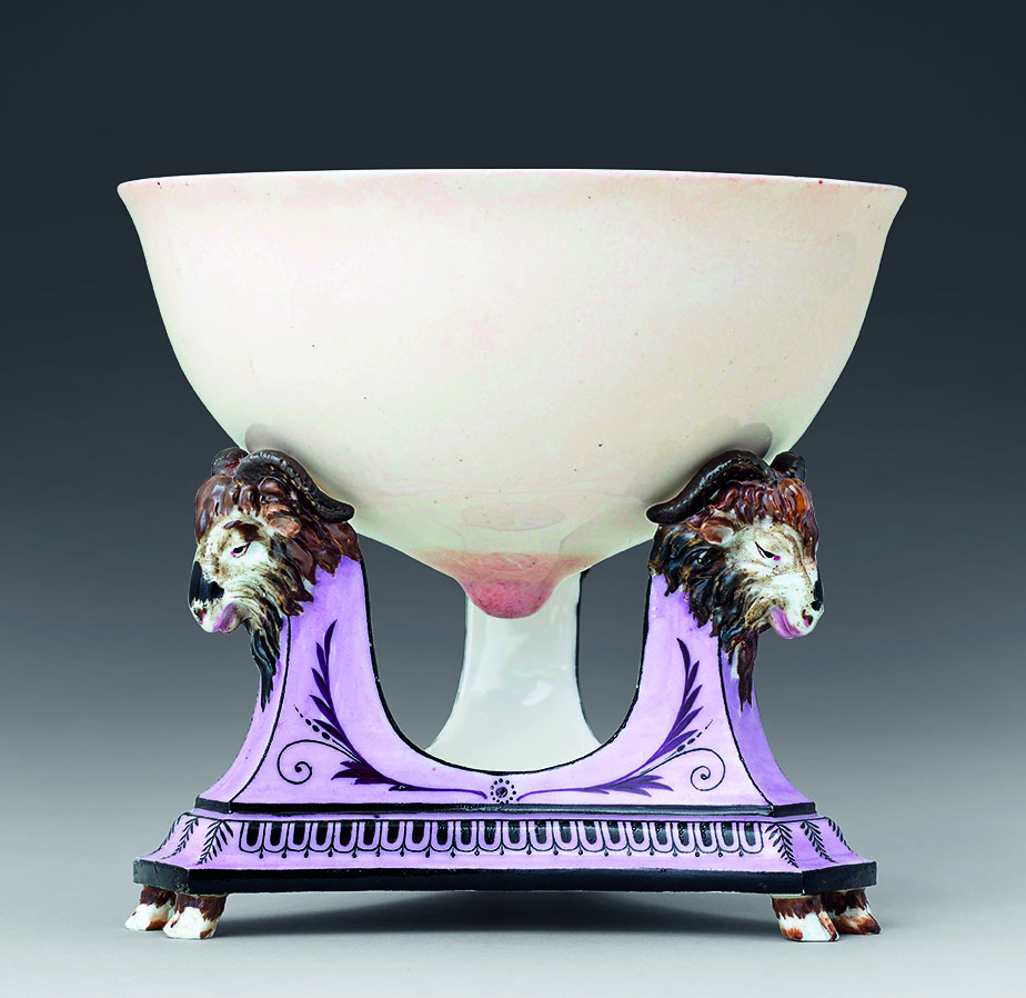 A decorative antique porcelain bowl with a white exterior, supported by a base adorned with two sculpted lion heads. The base features lavender and black detailing with intricate patterns, giving the piece an elegant and regal appearance.