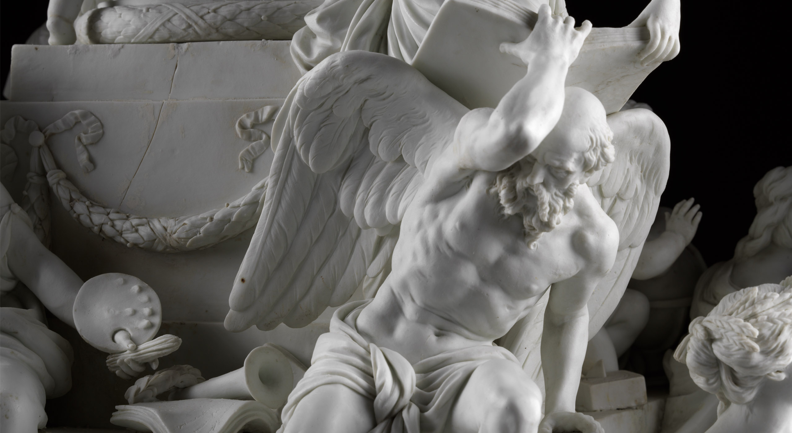 A detailed marble sculpture depicts a muscular, bearded man with wings, kneeling and holding up a heavy, rectangular object. The scene is dramatic with intricate carvings of ropes, shields, and other figures in the background. The figure's expression shows strain.