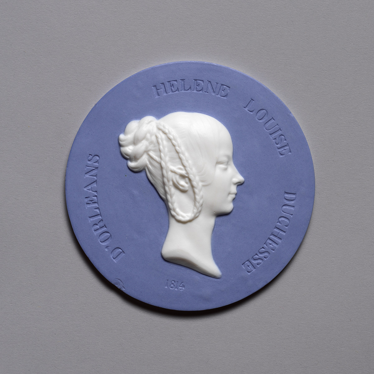 Blue and white medallion featuring a profile relief of a woman with intricately braided hair. The border reads "HELENE LOUISE DUCHESSE D'ORLEANS 1814.