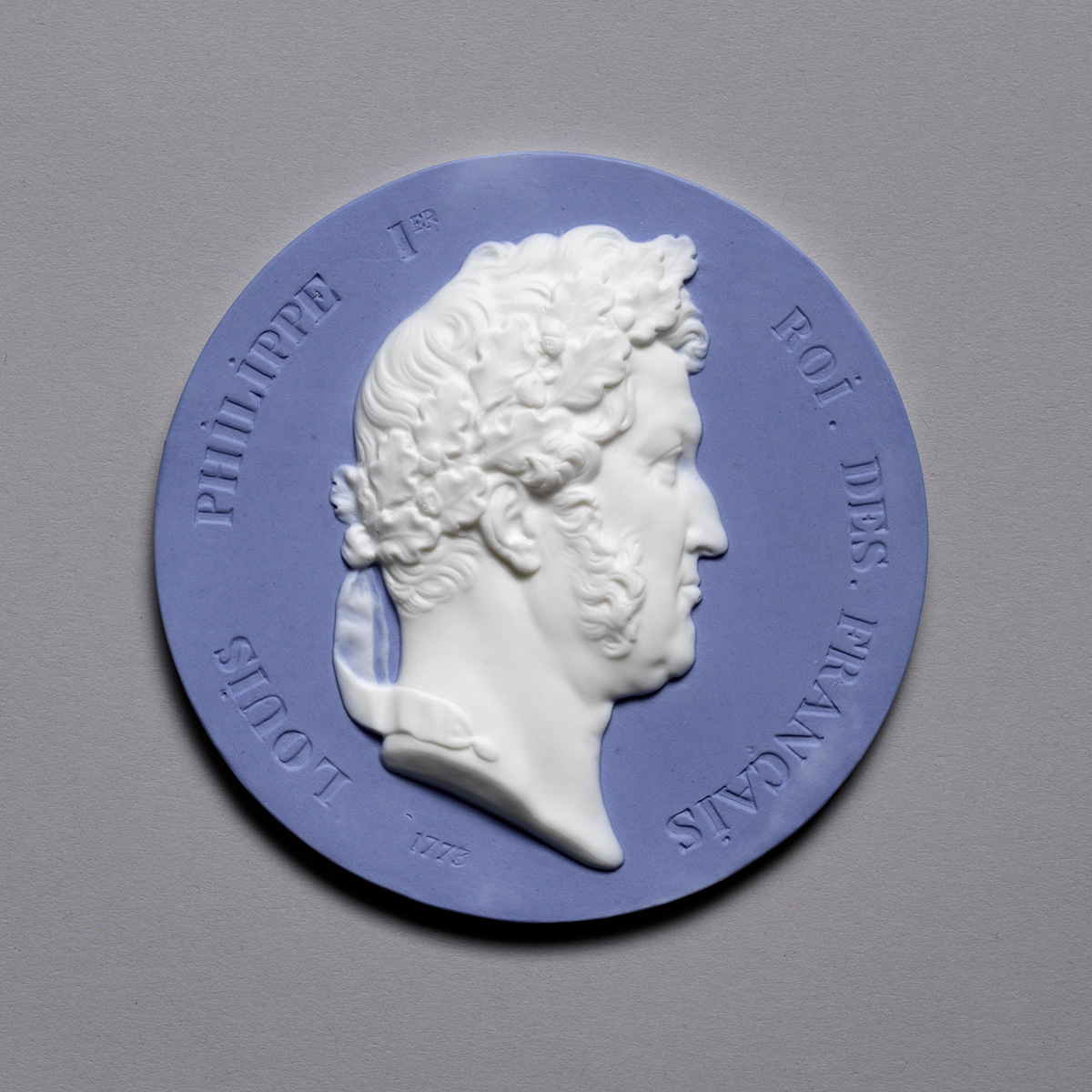 A blue and white medallion featuring a profile relief of a man's head. The text around the edge reads "Louis Philippe 1er, Roi des Français," indicating him as a king of France.