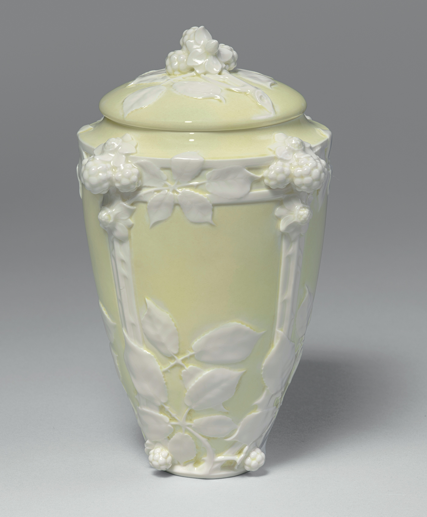 A pale yellow, lidded porcelain vase featuring an embossed design of leaves, branches, and flowers. The relief art is detailed and delicate, with raised floral motifs creating a textured look. The background displays a smooth, glossy finish.