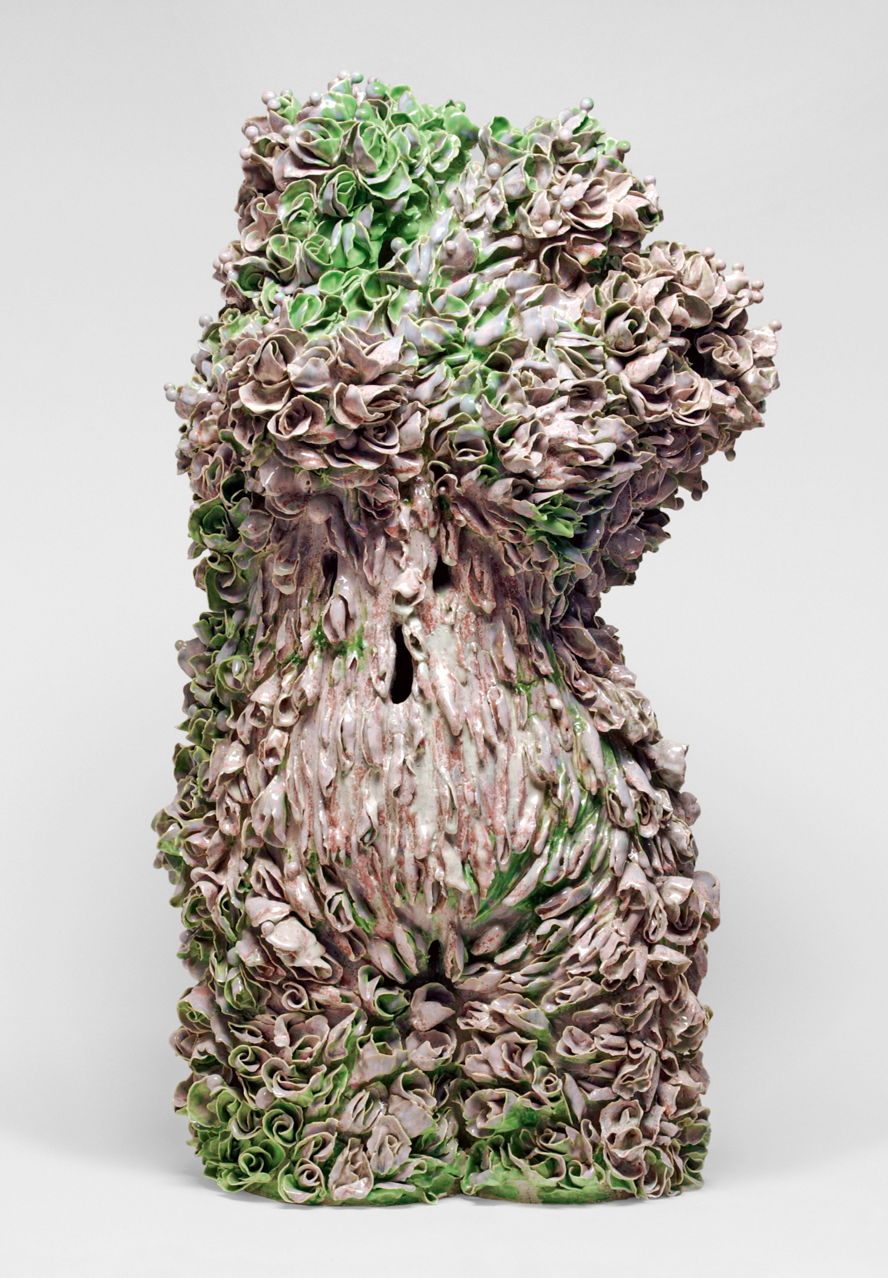 A ceramic sculpture resembling a human torso adorned with intricate swirls and folds. The sculpture features a blend of earthy tones and green highlights, giving it a textured, organic appearance reminiscent of plants or sea life. The background is plain white.