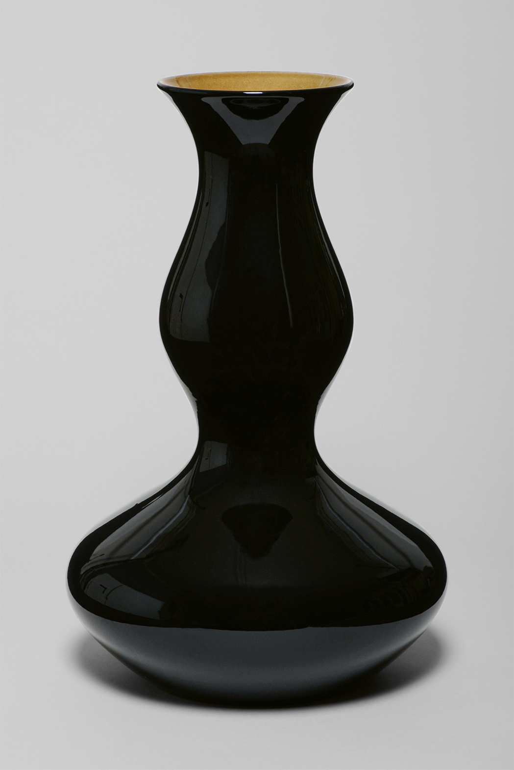 A black, glossy ceramic vase with a bulbous base, narrow neck, and slightly flared rim. The vase has a sleek and elegant design, reflecting light on its smooth surface. The interior of the vase is a contrasting light brown color. The background is plain white.