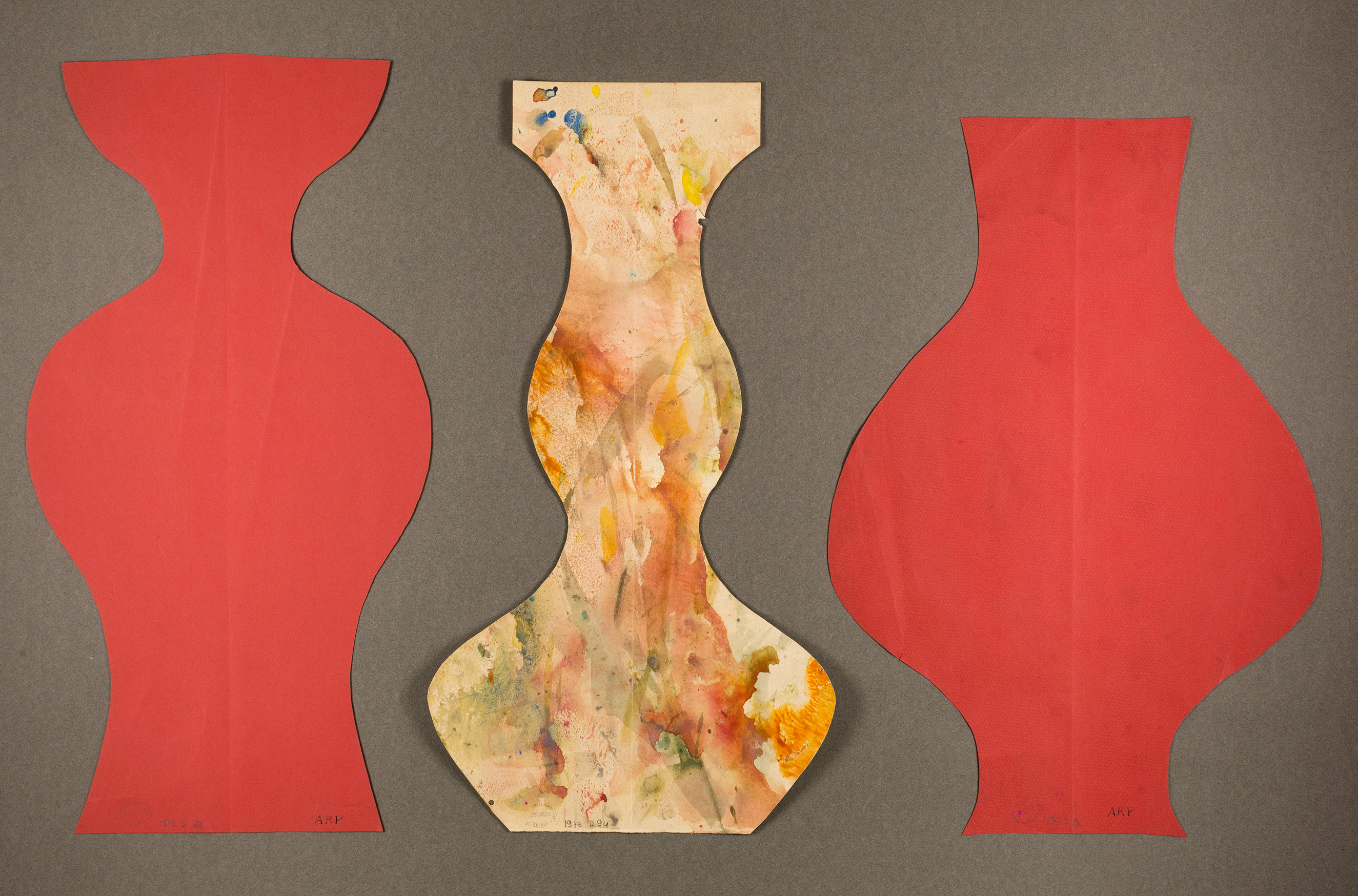 Three vase-shaped cutouts are displayed against a gray background. The cutouts on the left and right are red with smooth silhouettes, while the central cutout has a multicolored, paint-splattered design with a more intricate silhouette.