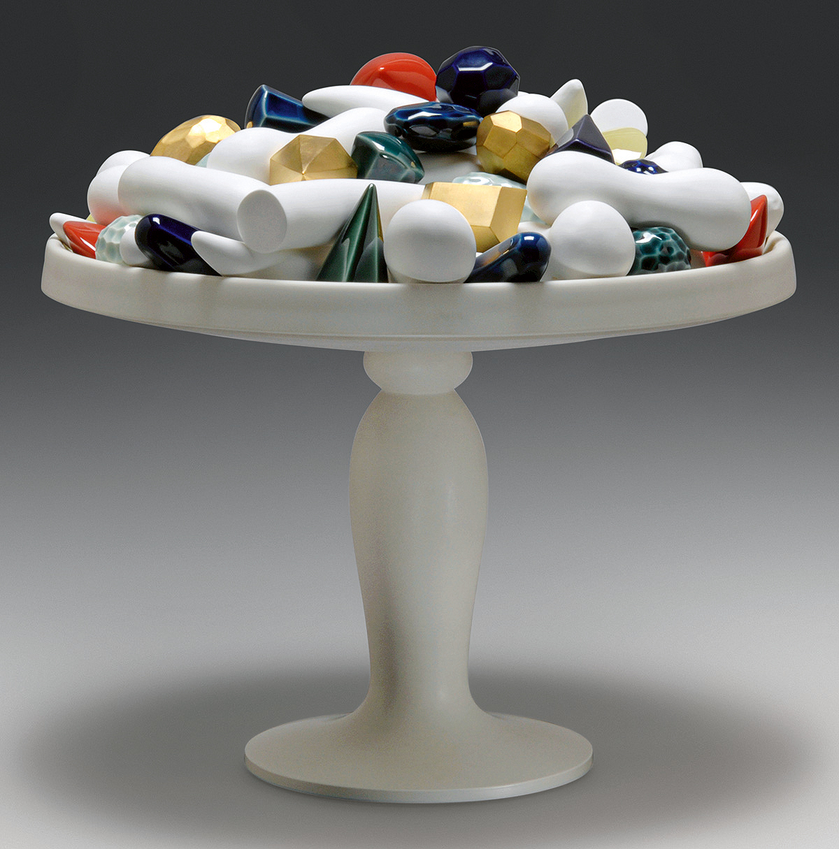 An artistic arrangement of various colorful geometric shapes and forms, including cylinders, spheres, and cones, displayed on a tall, elegant pedestal. The objects are shiny and vibrant, featuring colors like gold, blue, white, red, and green.A white pedestal dish holds an assortment of colorful geometric shapes, including cones, cylinders, spheres, and faceted objects, in various shades of blue, red, gold, green, and white. The background is a gradient of dark to light gray.