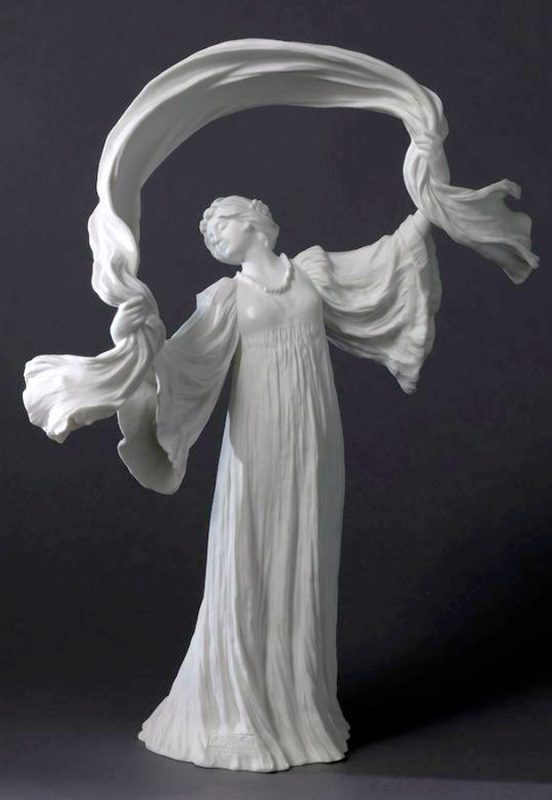 A porcelain sculpture of a robed woman with arms raised, holding flowing fabric above her head. The fabric and robe create a sense of movement against the dark background.