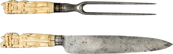 A carving fork and knife set with intricately carved ivory handles depicting human figures around the hilt and topped by a horse and rider.