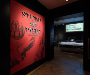 Title wall at the entrance of the "Staging the Table in Europe 1500-1800" exhibition. In the background several cases with objects are illuminated.