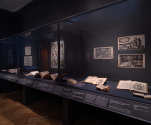 Detail of the "Staging the Table in Europe 1500-1800" exhibition featuring an enclosed case of illustrations and open books depicting carvers and carving instructions.